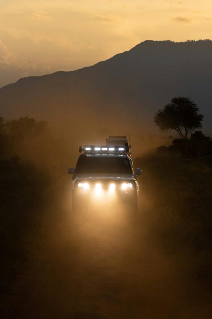 An off-road SUV drives through the dusty savannah of Tsavo, Kenya at sunset.